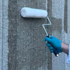 Worker in blue gloves using white paint roller on textured gray concrete wall