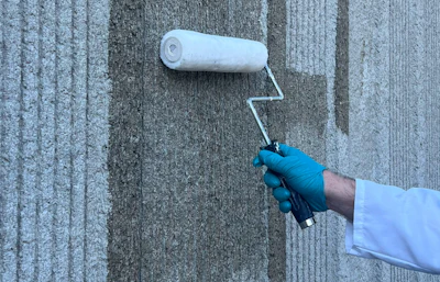 Worker in blue gloves using white paint roller on textured gray concrete wall