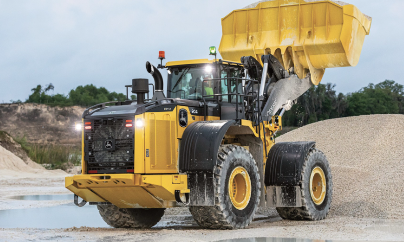 Yellow John Deere wheel loader dumping gravel at construction site with excavated hillside in background