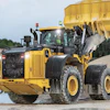 Yellow John Deere wheel loader dumping gravel at construction site with excavated hillside in background