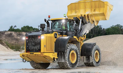 Yellow John Deere wheel loader dumping gravel at construction site with excavated hillside in background