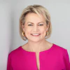 Professional headshot of a smiling woman with blonde hair wearing a magenta blouse