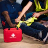 Workers in safety vests attending to an injured person with a red first aid kit nearby on the ground