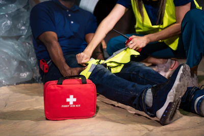 Workers in safety vests attending to an injured person with a red first aid kit nearby on the ground