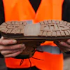Worker in orange safety vest holding up brown shoe sole with tread pattern