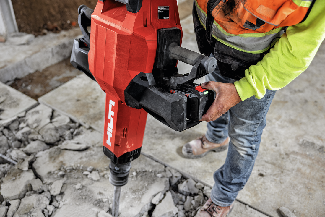 Construction worker using red Hilti pneumatic breaker on concrete surface