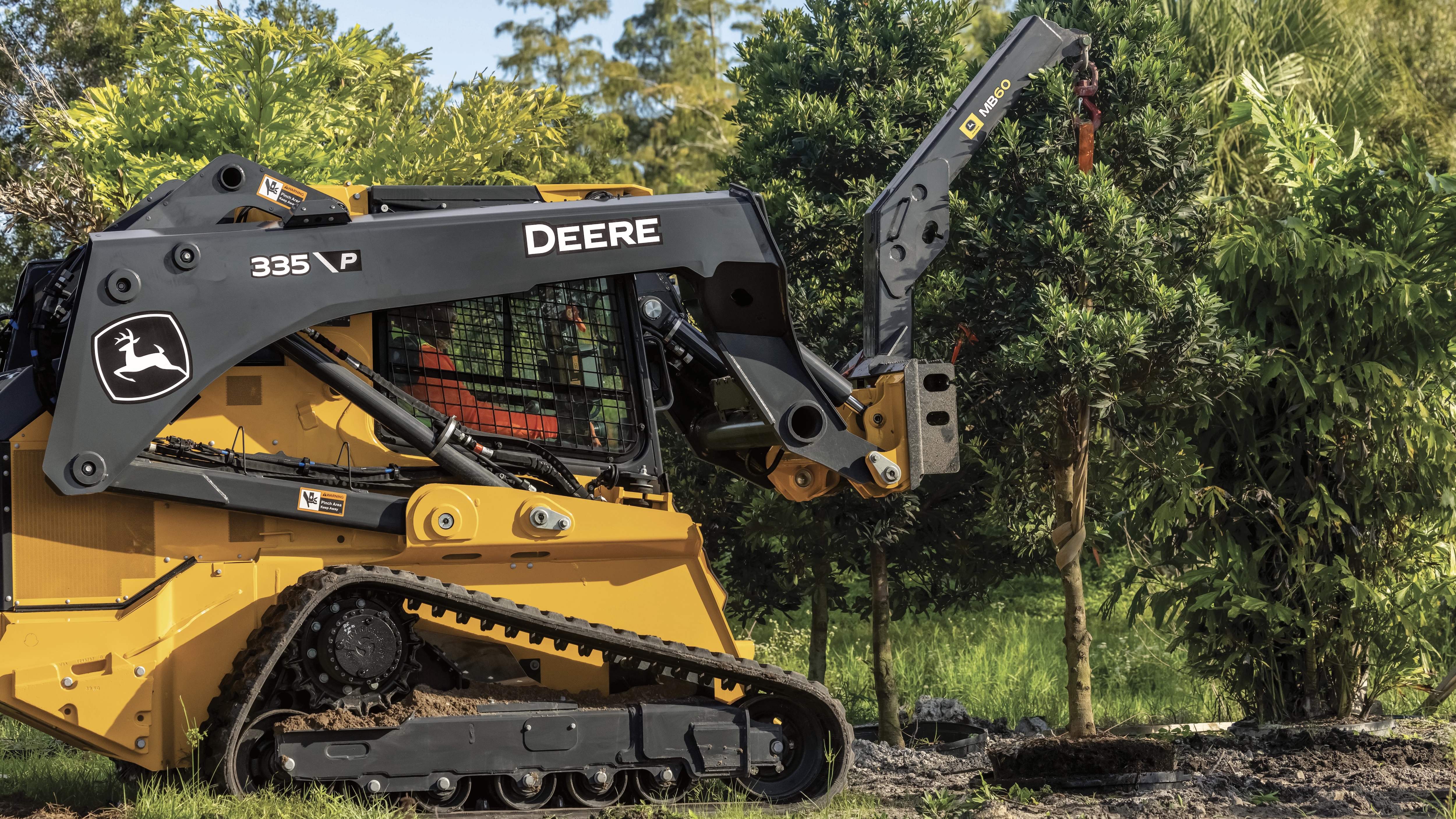 Yellow John Deere 335 skid steer loader with articulated boom arm operating near trees in outdoor setting