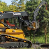 Yellow John Deere 335 skid steer loader with articulated boom arm operating near trees in outdoor setting
