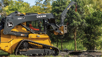 Yellow John Deere 335 skid steer loader with articulated boom arm operating near trees in outdoor setting