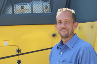 Professional man in blue shirt standing in front of yellow and blue vehicle
