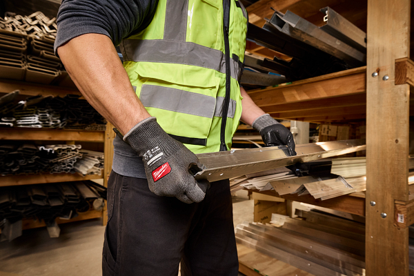 Construction worker wearing neon safety vest and work gloves handling wood materials in warehouse