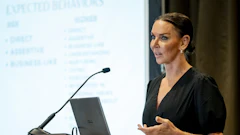 Professional woman speaking at podium during business presentation with projected content visible