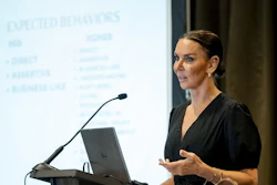 Professional woman speaking at podium during business presentation with projected content visible