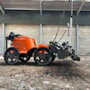 Orange and black agricultural tractor with attached hydraulic implement in industrial yard