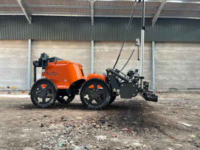 Orange and black agricultural tractor with attached hydraulic implement in industrial yard