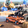 Operator demonstrates zero-turn mower at outdoor equipment event with construction machinery in background