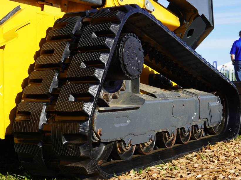 Close-up of yellow excavator track and undercarriage with metal cleats on sandy ground