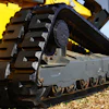 Close-up of yellow excavator track and undercarriage with metal cleats on sandy ground