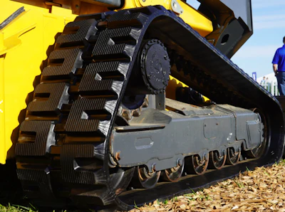 Close-up of yellow excavator track and undercarriage with metal cleats on sandy ground