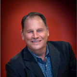 Professional headshot of a smiling man in business casual attire against a red background