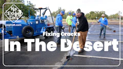 Asphalt repair crew filling cracks in desert parking lot with blue equipment and workers