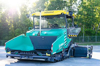 Turquoise VÖGELE asphalt paver with yellow crane attachment parked outdoors near trees