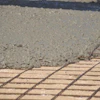 Wet concrete being poured over metal reinforcement mesh during construction flooring work