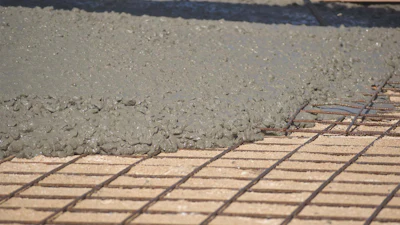 Wet concrete being poured over metal reinforcement mesh during construction flooring work