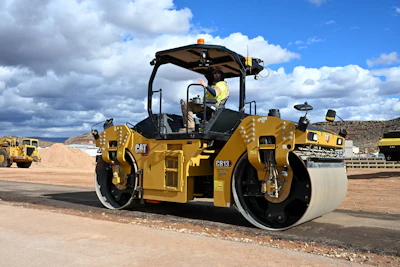 Yellow Caterpillar CB13 asphalt roller compactor with operator in hard hat on construction site