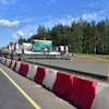 Highway construction site with concrete paving machine and red-white safety barriers along roadside