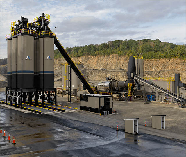 Industrial concrete batch plant with tall storage silos and conveyor systems at an active quarry site