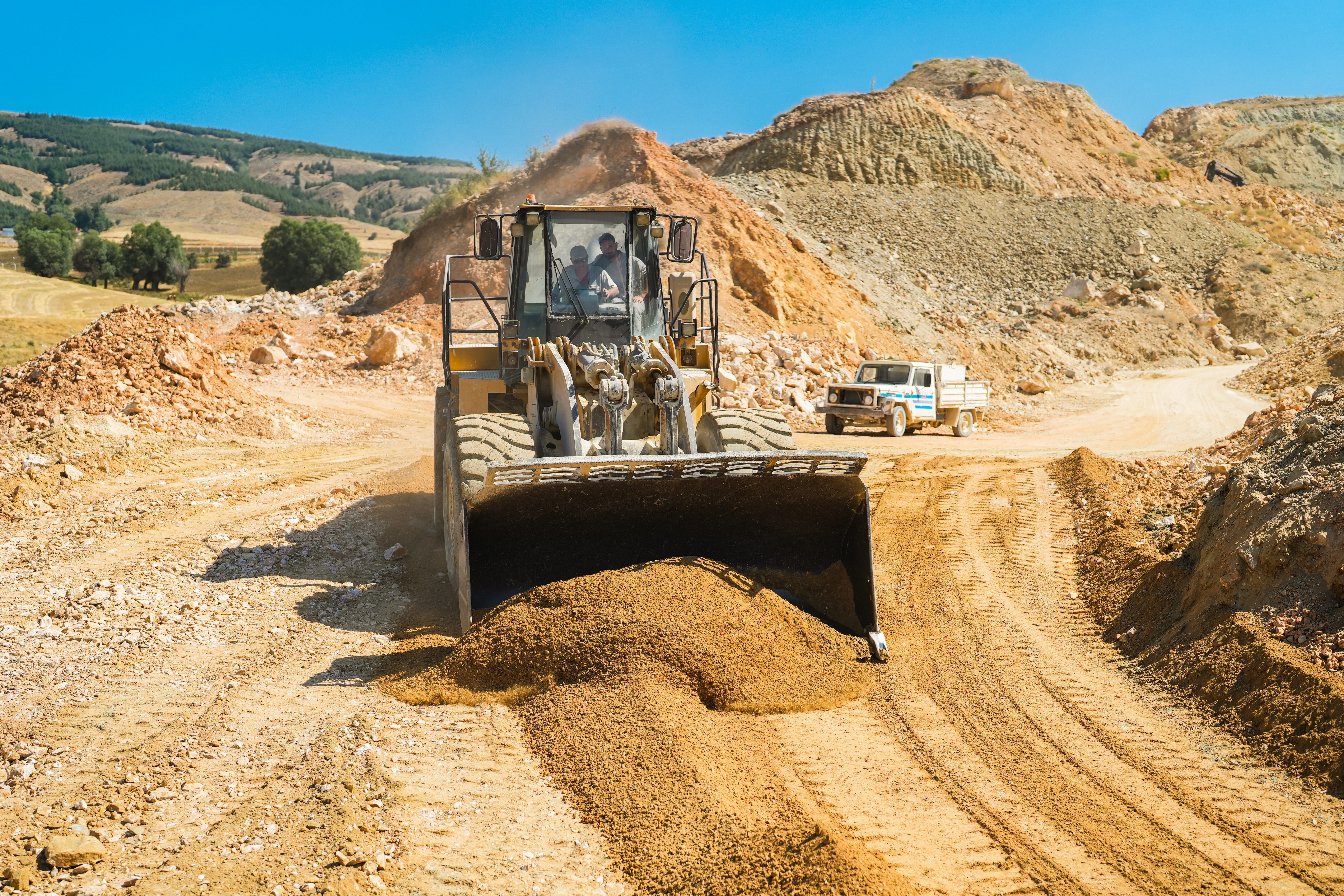 Bulldozer moving gravel at a quarry with piles of earth and equipment visible on a sunny day