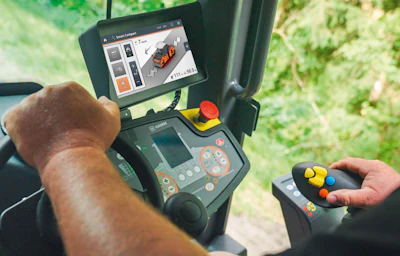 Operator holding remote control for heavy machinery with digital display screen showing equipment interface outdoors