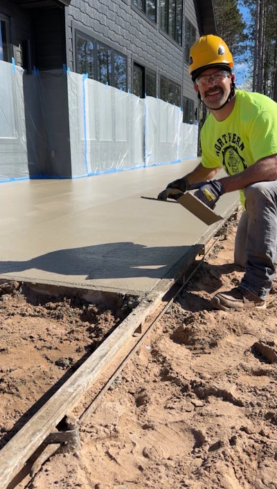 Construction worker smoothing wet concrete foundation at residential building site with safety equipment