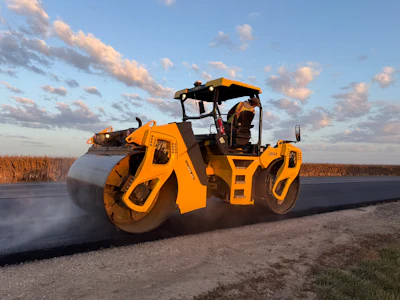 Yellow asphalt roller compacting fresh pavement on rural road construction site