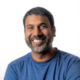 Smiling man with dark beard wearing blue t-shirt against white background
