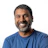 Smiling man with dark beard wearing blue t-shirt against white background Headshot