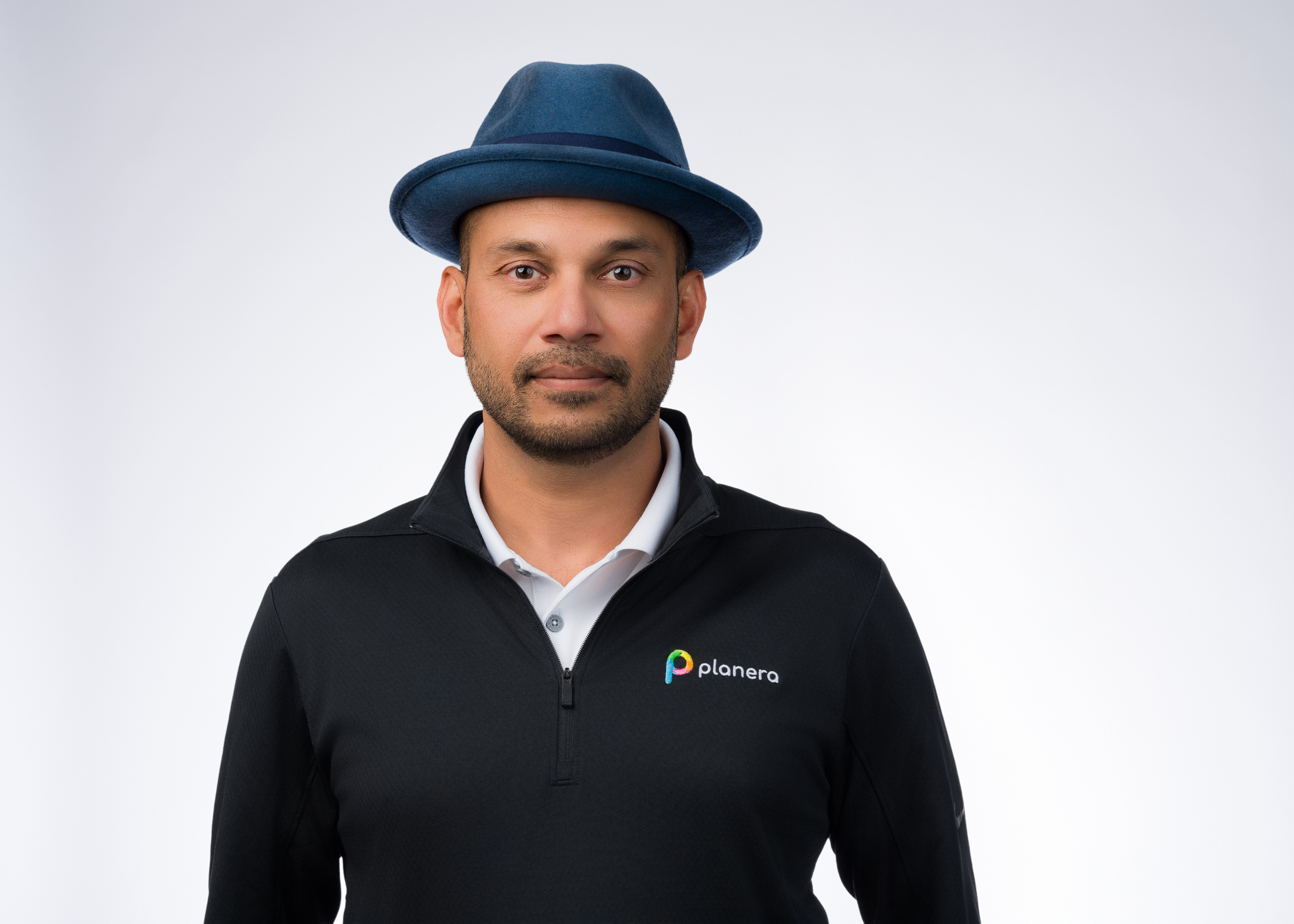 Professional man wearing blue fedora and black Planera-branded jacket over white shirt Headshot
