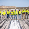 Team of construction workers in yellow safety vests and hard hats standing on airport runway with desert landscape
