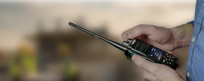 Person holding a black two-way radio with antenna outdoors