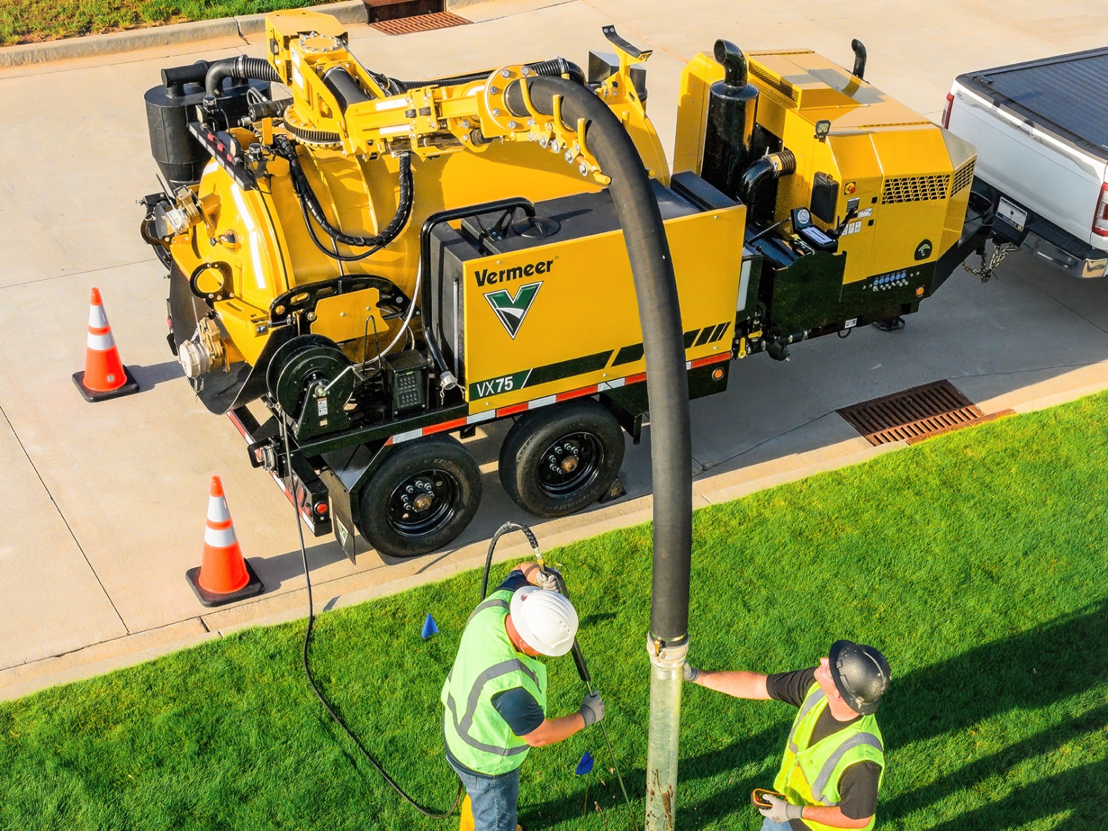 Two utility workers in safety gear operating Vermeer industrial equipment on a residential street.