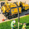 Two utility workers in safety gear operating Vermeer industrial equipment on a residential street.