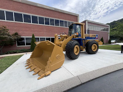 Yellow and blue wheel loader with bucket attachment parked in front of brick industrial building