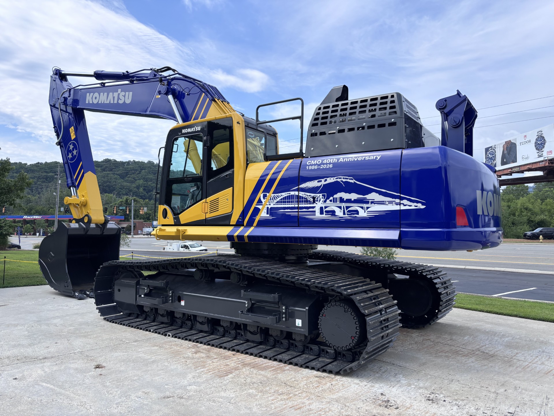 Blue and yellow Komatsu excavator next to Ohio Steel branded trailer at outdoor equipment display