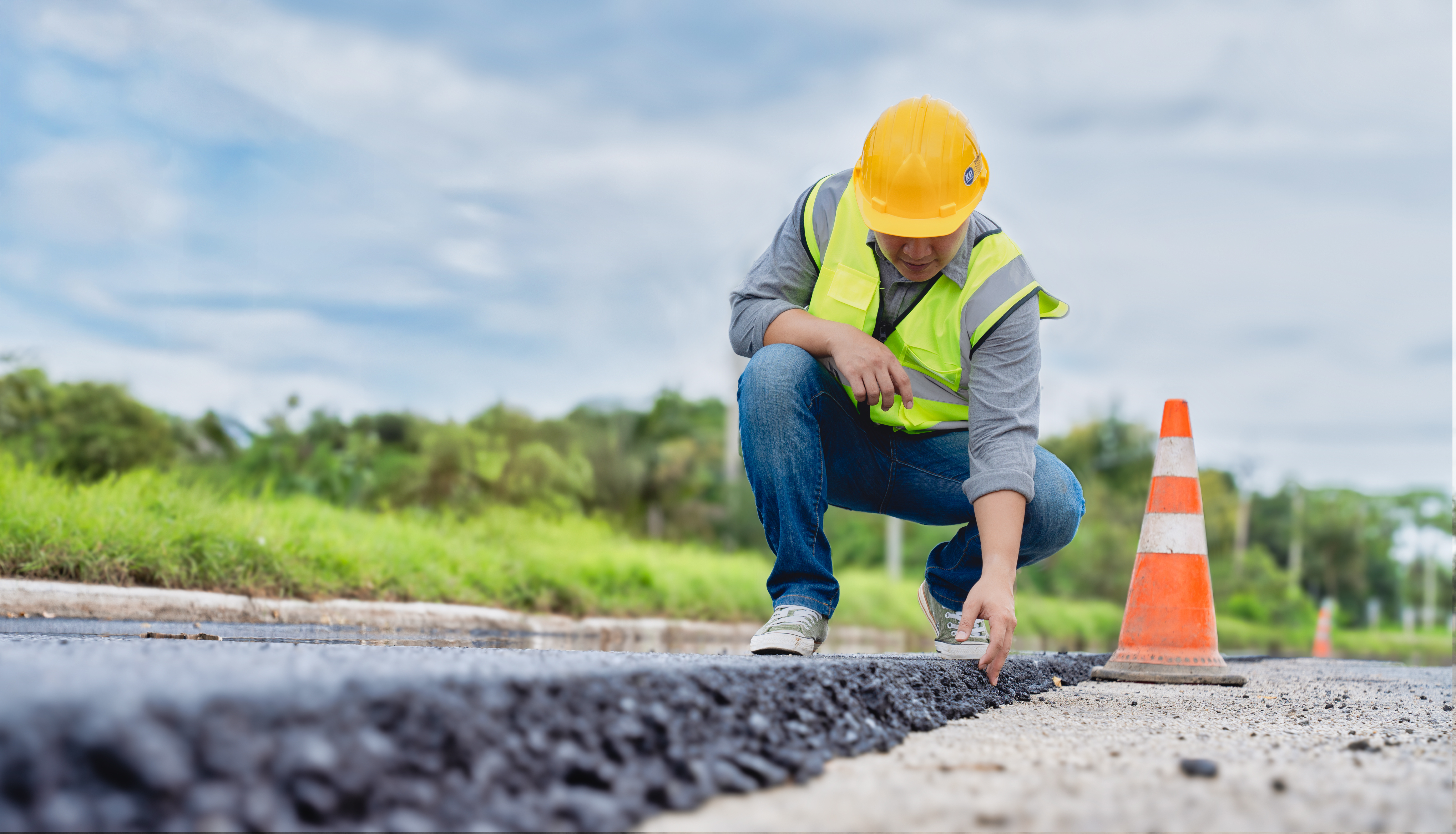 Construction worker in safety gear inspecting asphalt pavement on a road project