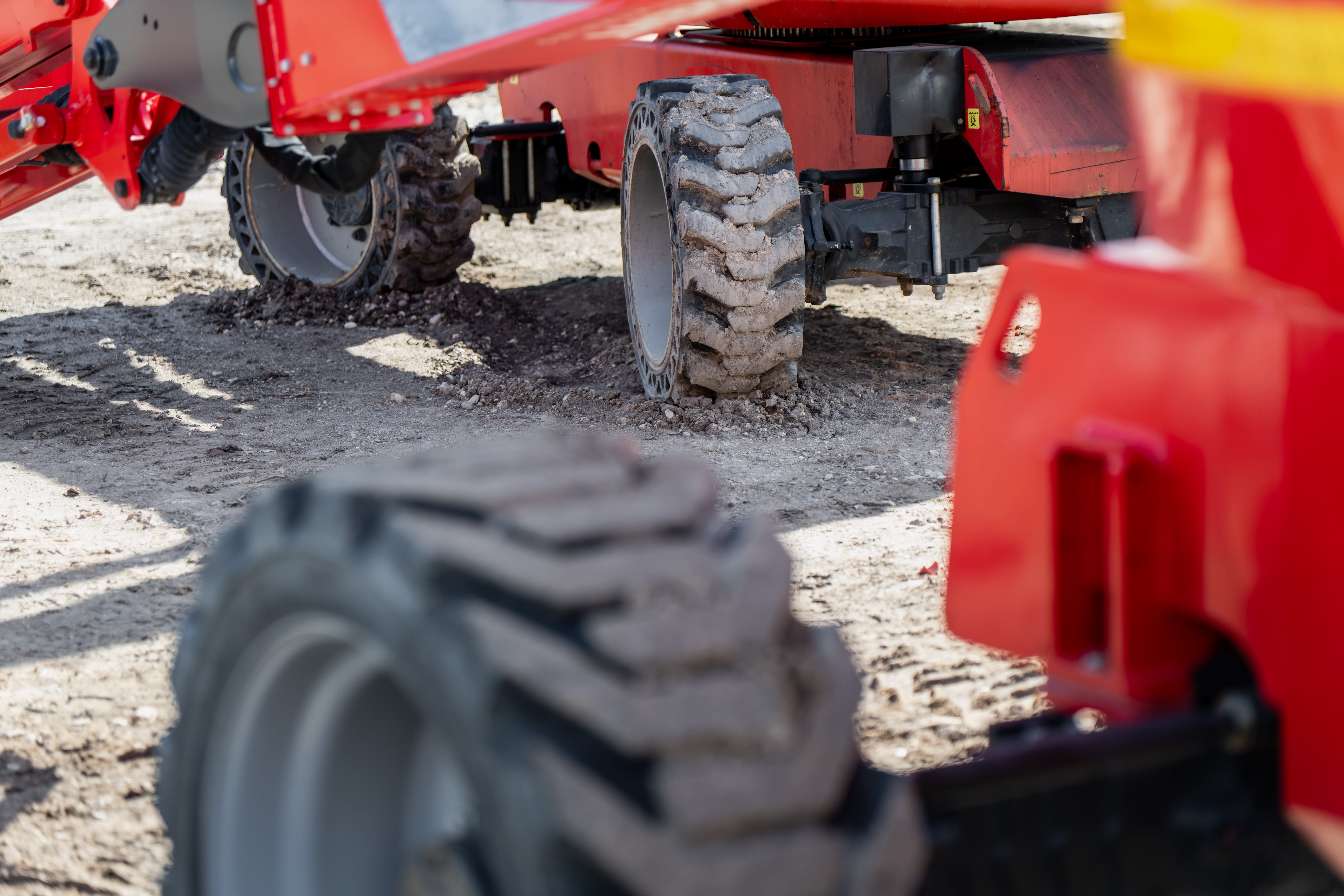 Red agricultural equipment with large tires parked on sandy ground