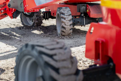 Red agricultural equipment with large tires parked on sandy ground
