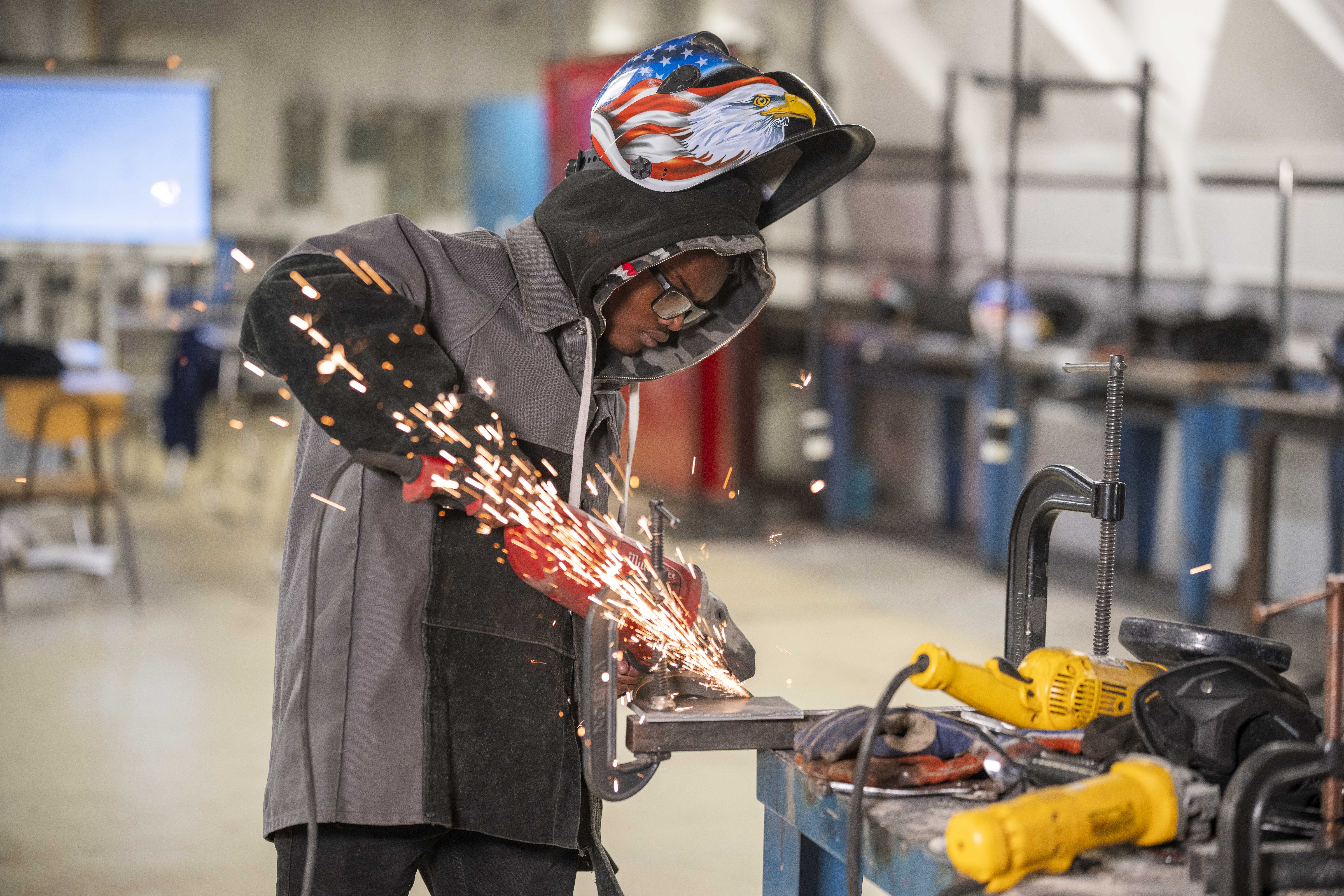 Welder in protective gear performing metal welding with sparks in an industrial workshop