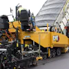 Yellow Caterpillar asphalt paver and dump truck at construction site with workers in safety gear