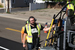 Construction worker in safety vest operating yellow equipment on residential street